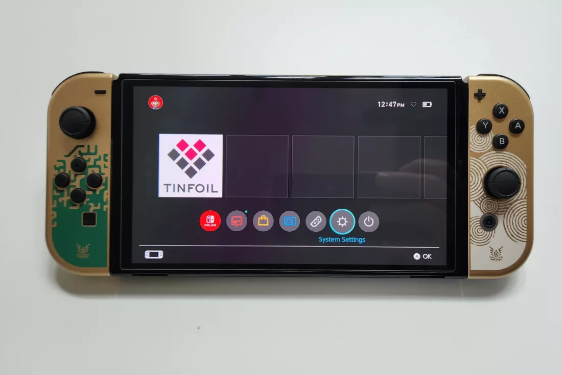 Una consola Nintendo Switch con un diseño personalizado inspirado en The Legend of Zelda, mostrando en pantalla la aplicación Tinfoil en el menú principal. La consola tiene controladores decorados con símbolos dorados y patrones únicos.